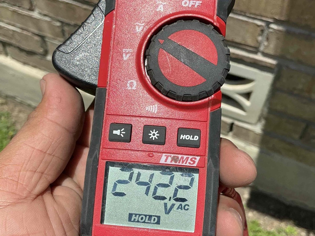 Clamp meter showing 242.2 volts AC measured at a residential solar system during inspection