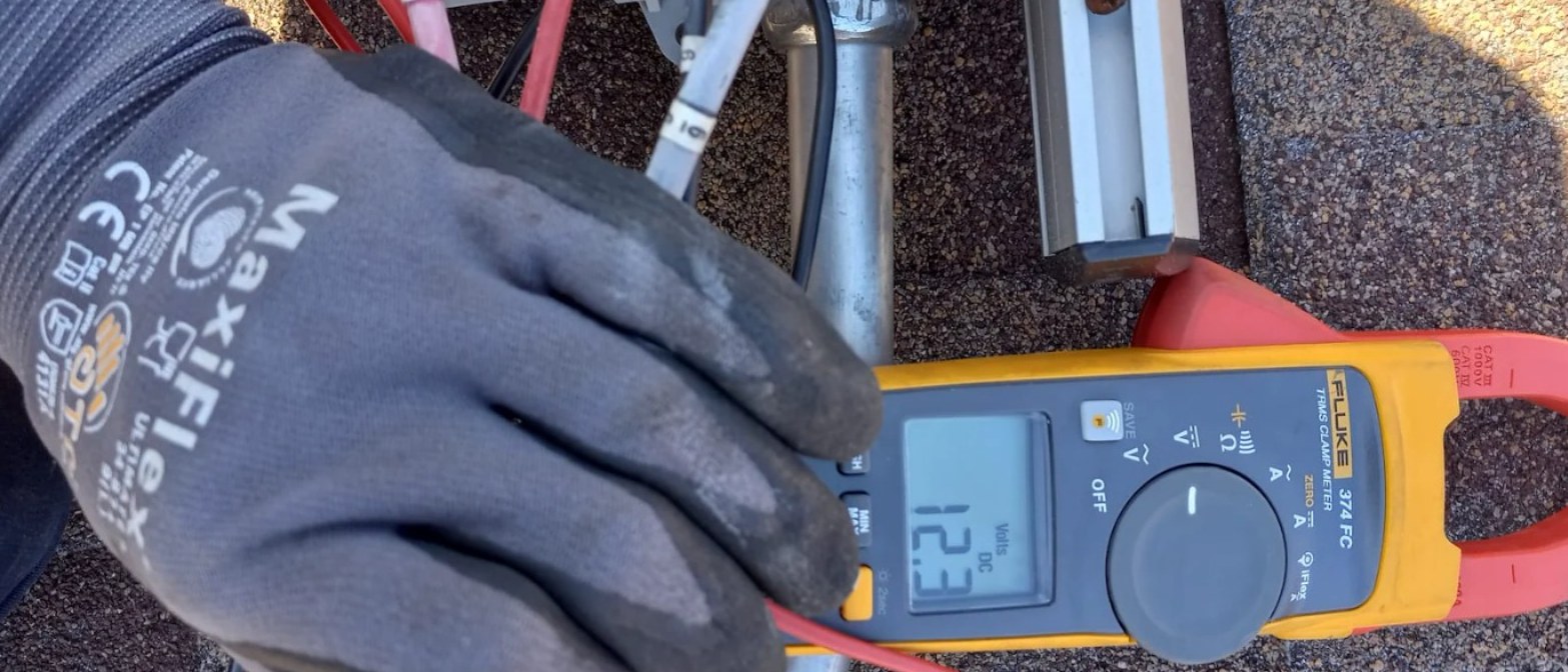 Solar Service technician testing optimizer output with a clamp meter