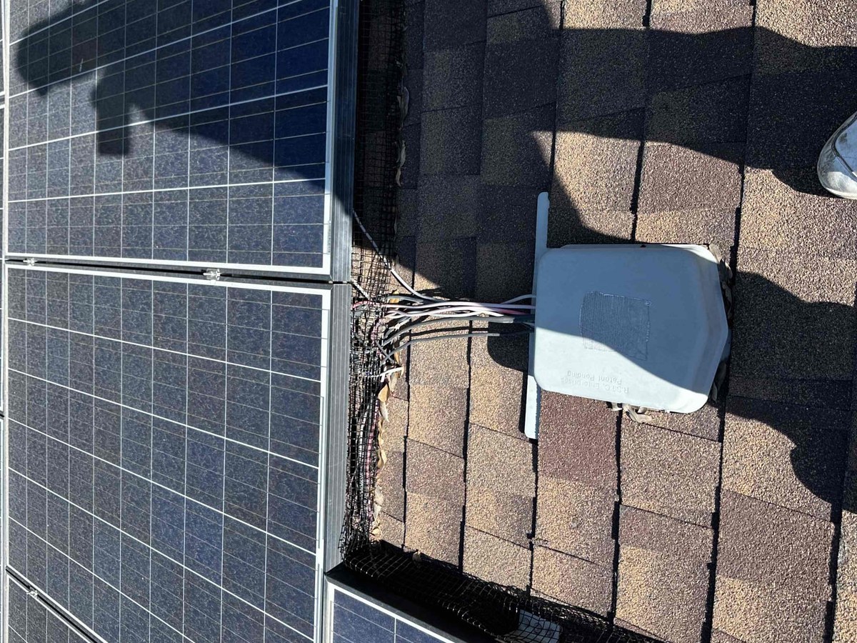 Edge of a rooftop solar array showing wiring and a junction box during maintenance